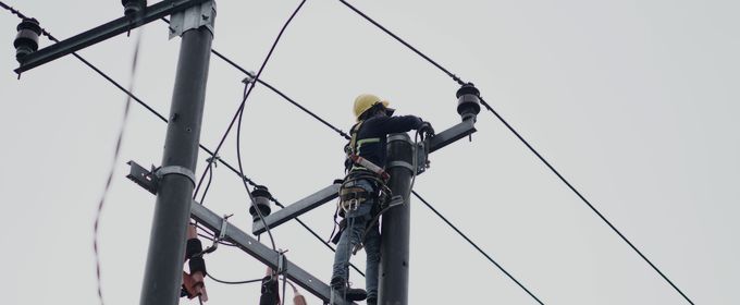 A line worker aloft in a web of distribution conductors
