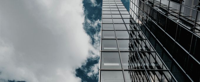 A glass office tower against moving clouds